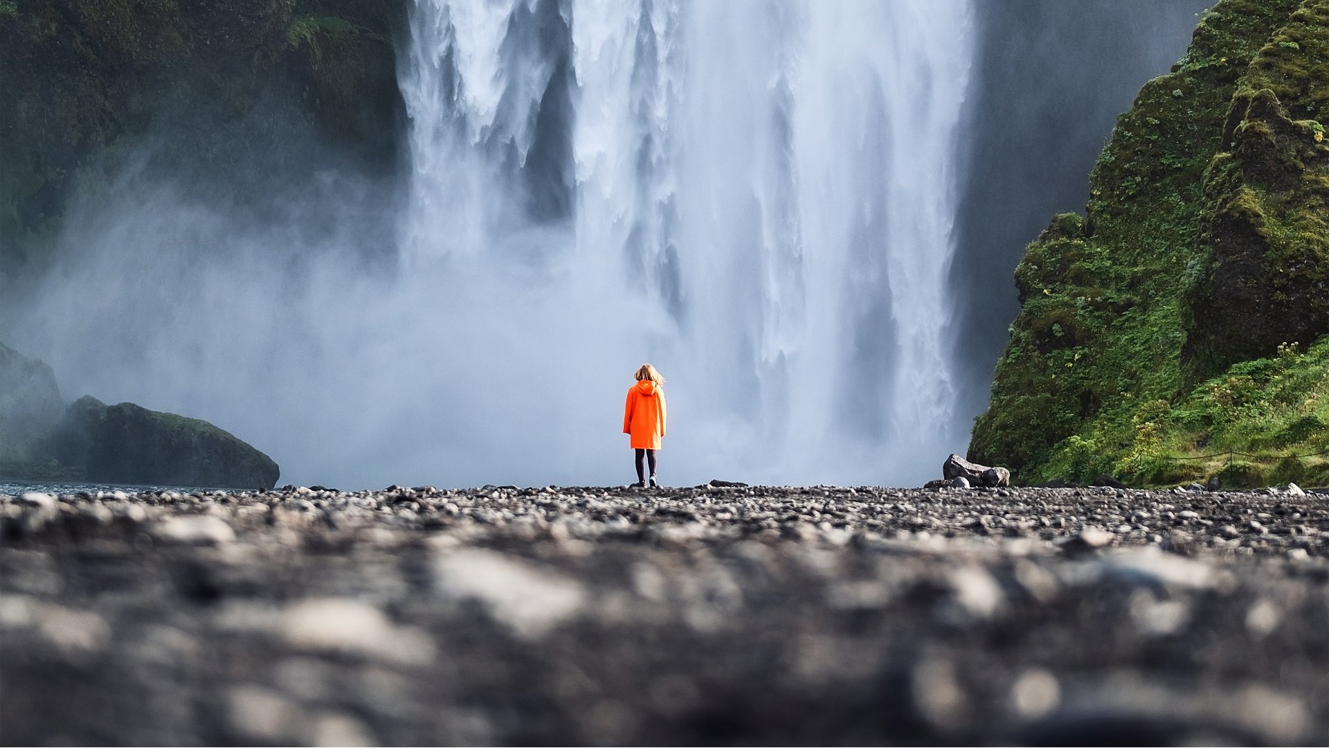 Person standing under Skógafoss waterfall, South Iceland 